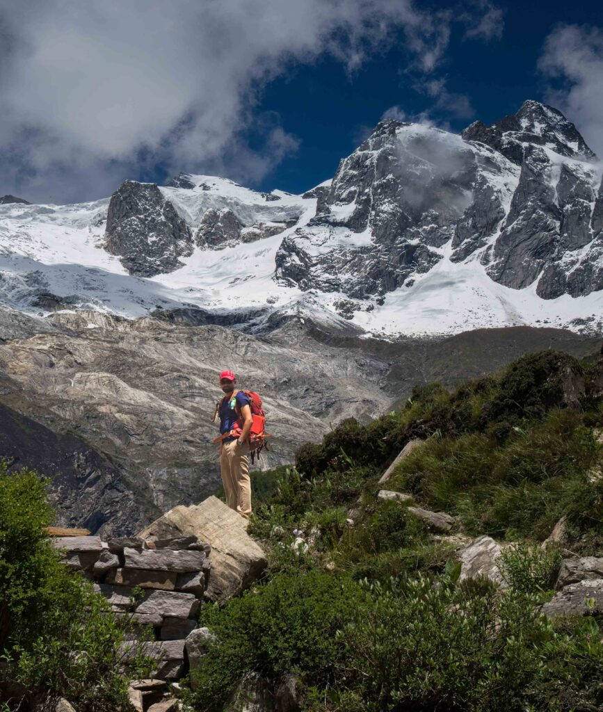 A person looking towards the camera in front of mountain scenery